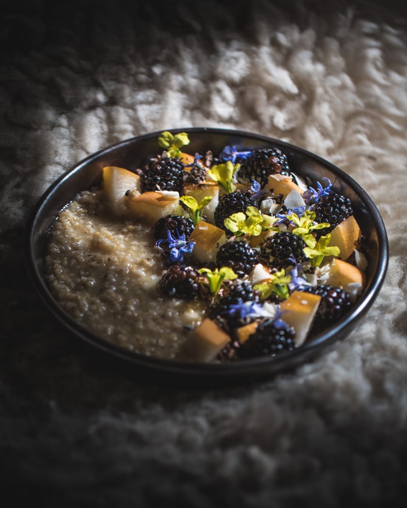 Bowl of perfectly cooked steel cut oats topped with Asian pear, blackberries and flowers.