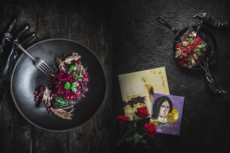 Hands wearing black vinyl gloves handling pulled pork with Trent Reznor painting.
