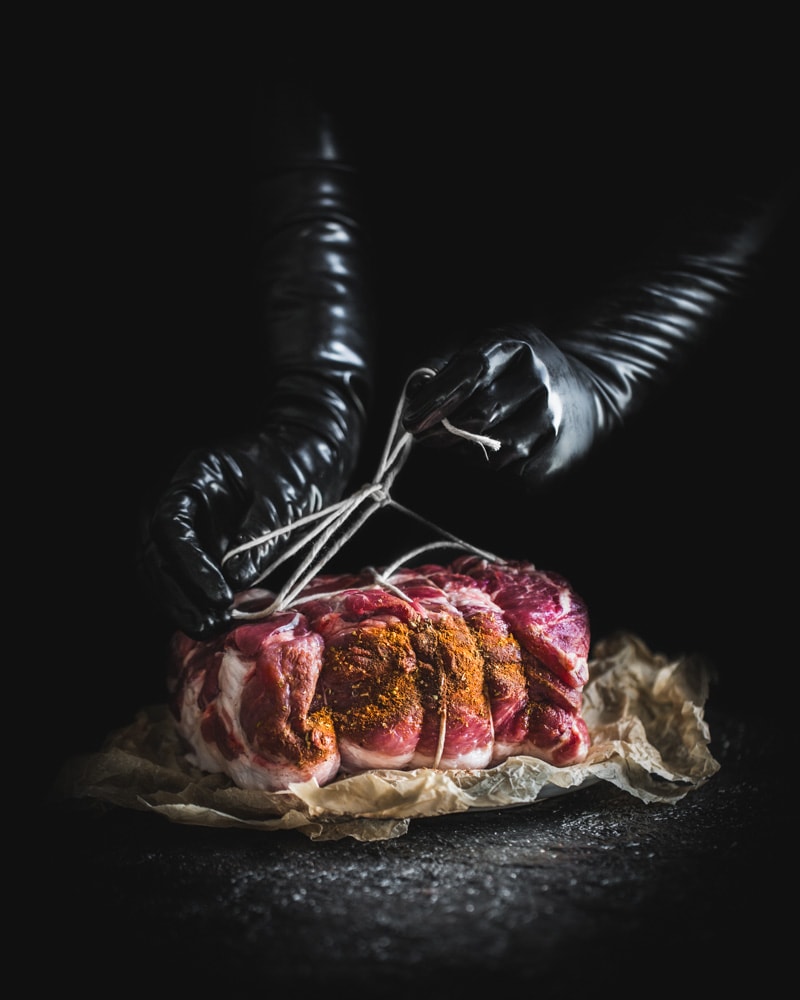 Meat being tied up by hands in black vinyl gloves